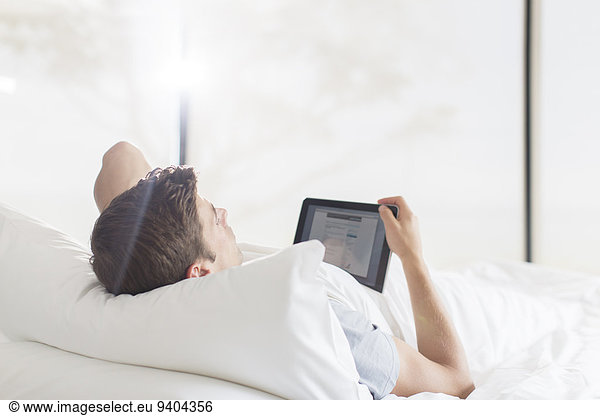 Young man lying on bed and using tablet