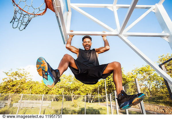 Young man on basketball court  swinging on basketball net frame  low angle view