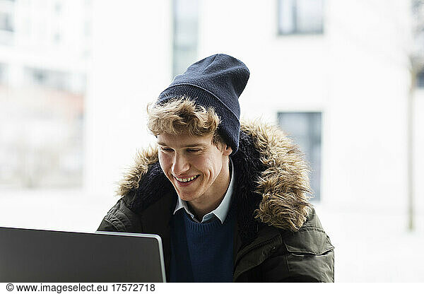 young man outside with winter cap and laptop in winter