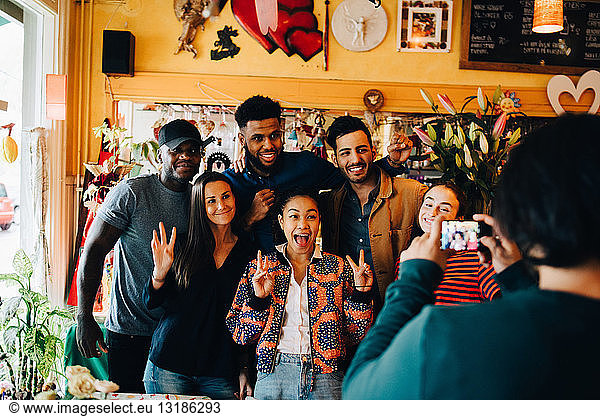 Young man photographing cheerful multi-ethnic friends standing at restaurant during brunch