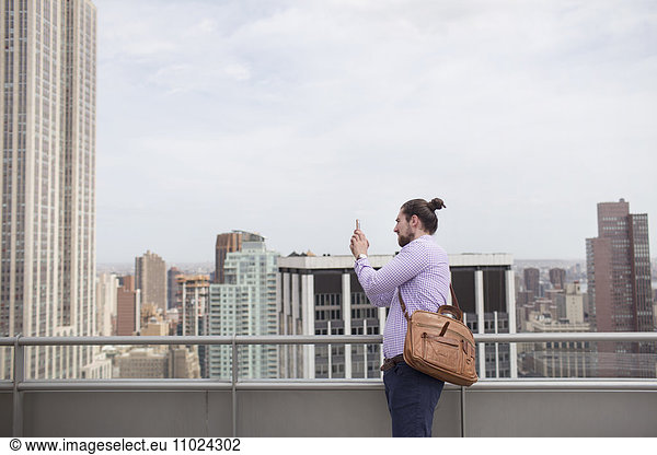 Young man photographing city view while standing at rooftop restaurant