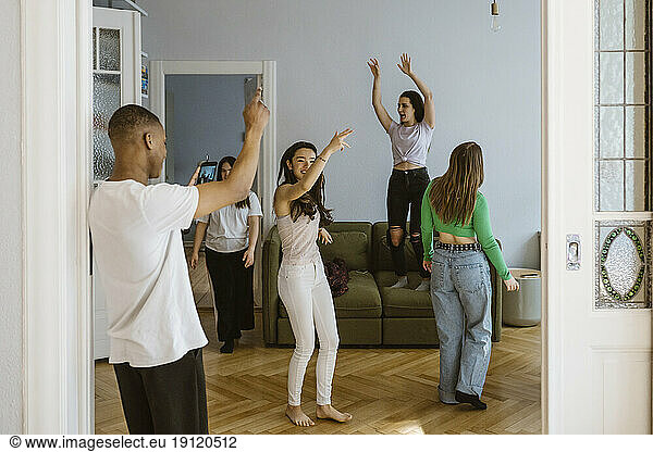 Young man photographing female friends dancing in living room at home
