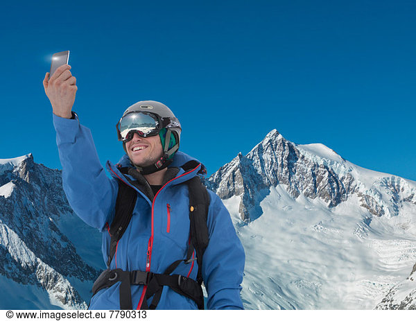 Young man photographing self on smartphone in mountains