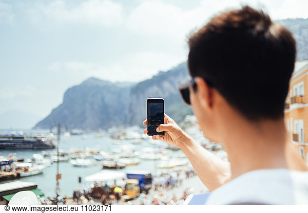 Young man photographing through smart phone at Marina Grande against sky