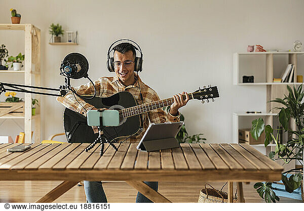 Young man playing guitar and podcasting at home