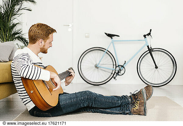 Young man playing guitar in living room at home