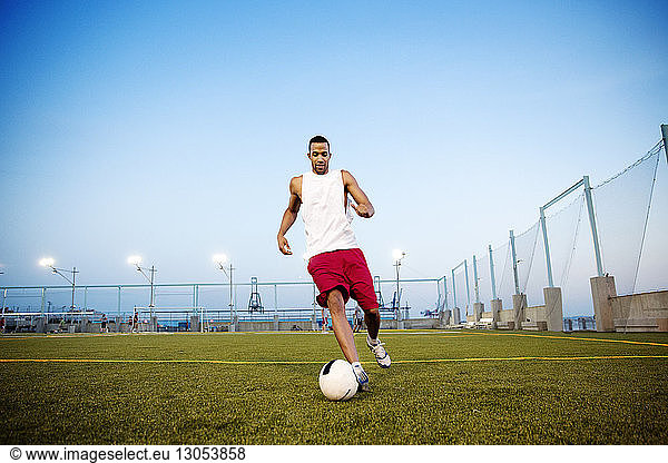 Young man playing soccer on field against clear sky