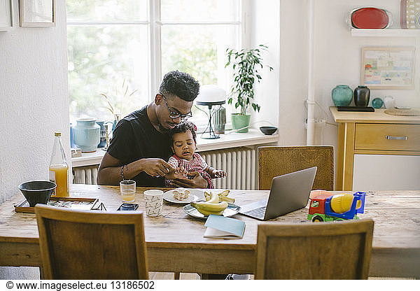 Young man playing with daughter while sitting at table in house