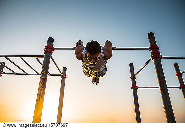 Young man practicing calisthenics at an outdoor gym at sunrise