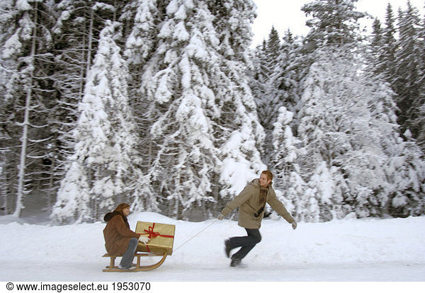 Young man pulling woman on sledge with Christmas gift