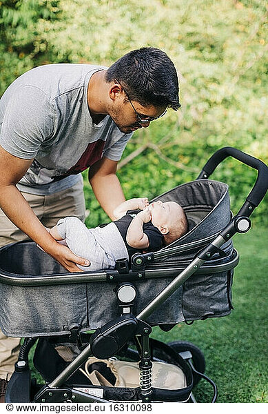 Young man putting baby boy in carriage at park