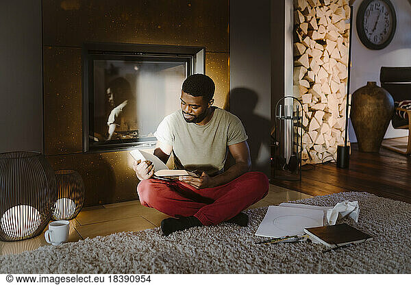 Young man reading book while sitting cross-legged at home