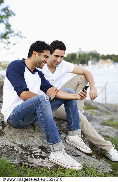 Young man reading text message with friend outdoors