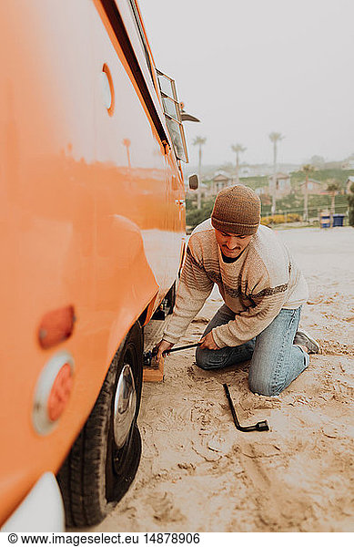 Young man removing flat tyre on recreational vehicle at beach  Jalama  California  USA