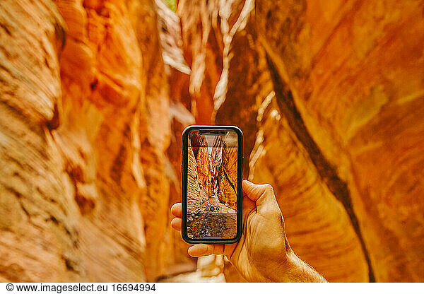 Young man's hand taking picture of slot canyons in Kanarra Falls