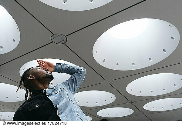 Young man shielding eyes looking at illuminated ceiling