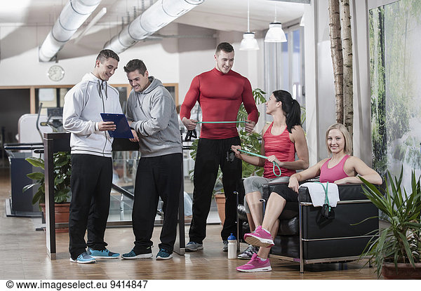 Young man showing clipboard to friends in gym