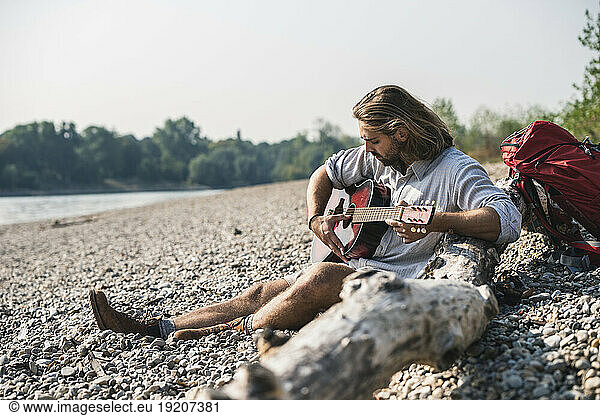Young man sitting at the riverside playing guitar