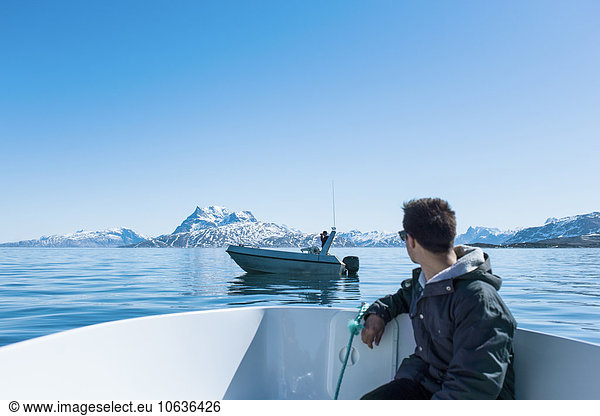 Young man sitting in boat looking at snowcapped mountains
