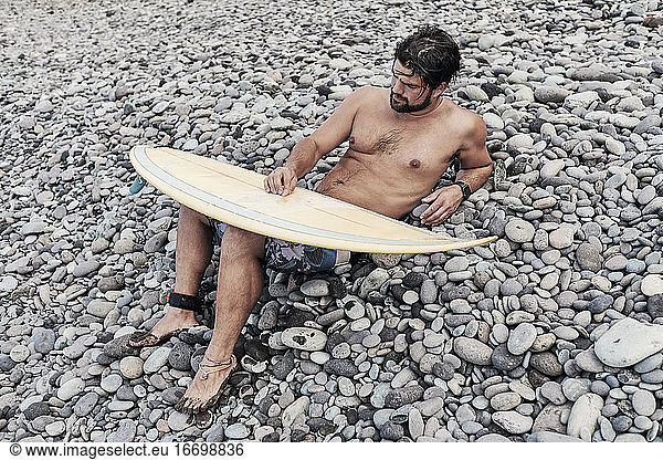 Young Man Sitting Near Surf Board and Resting
