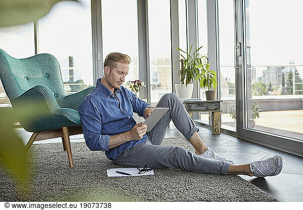 Young man sitting on carpet at home using tablet