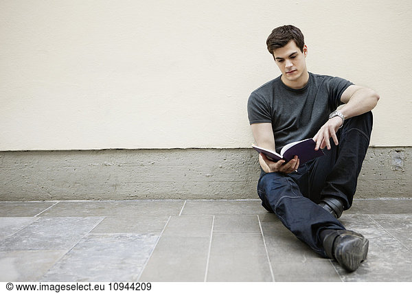 Young man sitting on floor reading a book