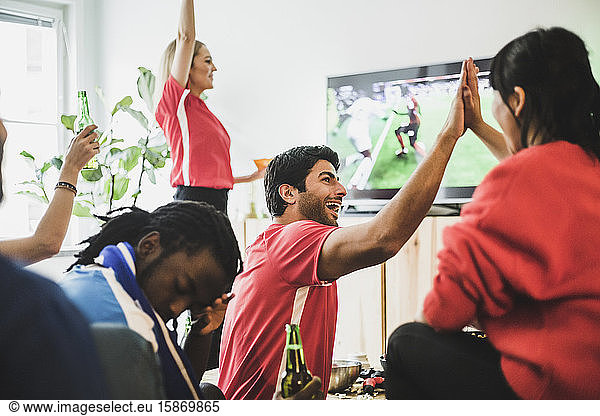 Young man sitting upset while red team celebrating victory at home