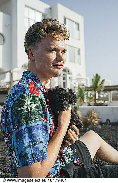 Young man sitting with cute dog in front yard