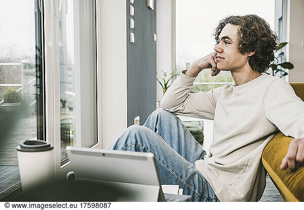 Young man sitting with hand on chin by on sofa in living room