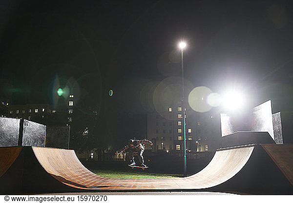 Young man skateboarding on ramp at skate park at night