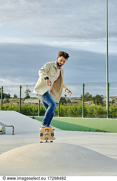 Young man skates at a skate park in casual clothes