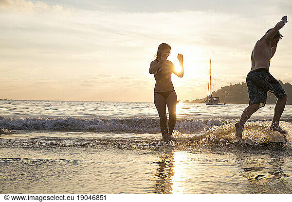 Young man skim boards along beach  girl watches
