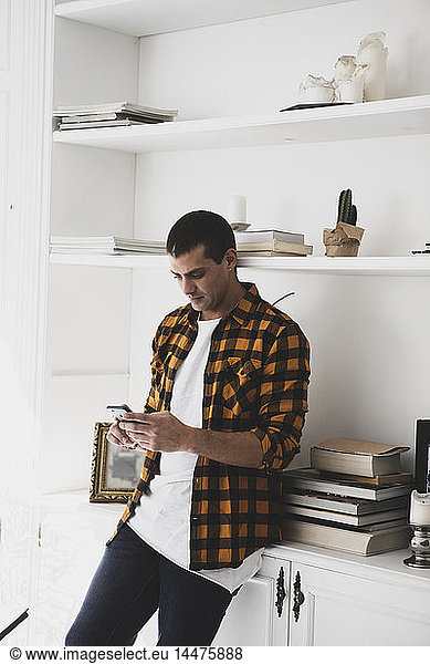 Young man standing at a shelf using cell phone
