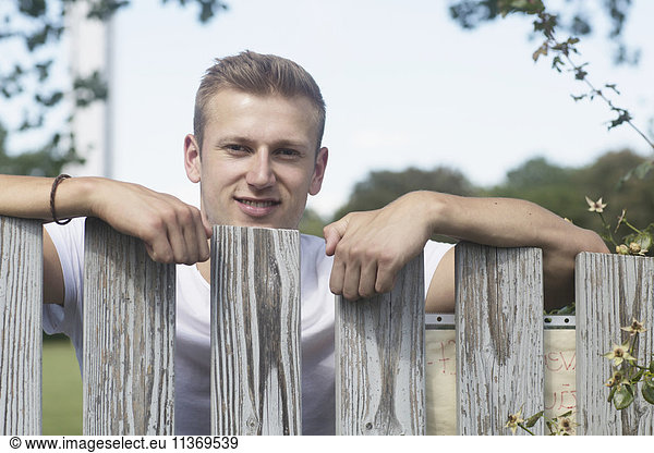 Young man standing by wooden fence in urban garden