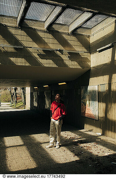 Young man standing in sunlight below underpass