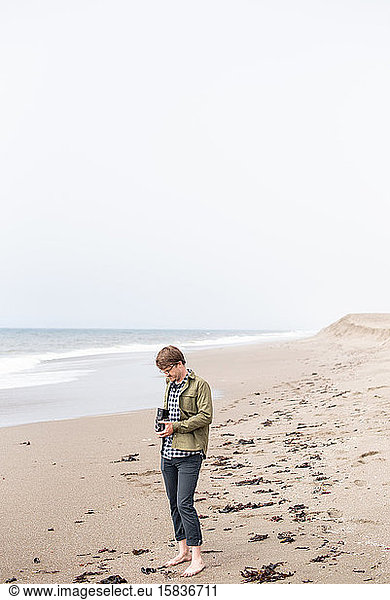Young man standing on beach taking photograph with film camera