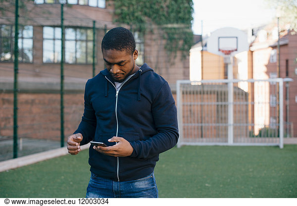 Young man standing on playing field while using smart phone