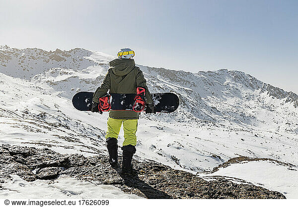 Young man standing on rock with snowboard