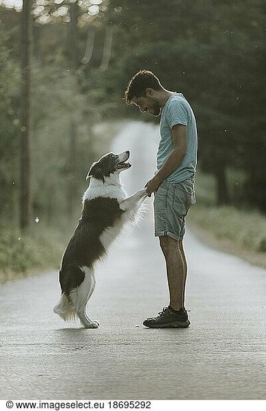 Young man standing with dog on road at sunset