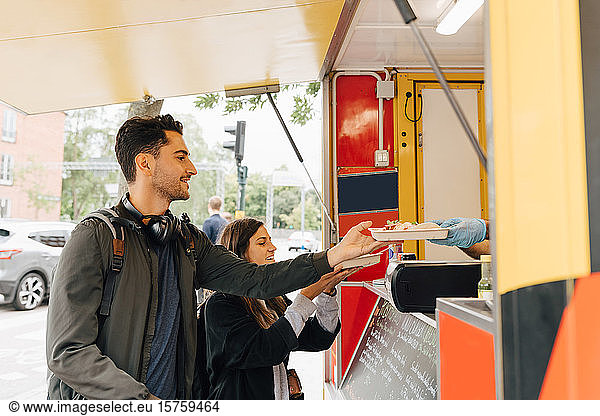 Young man standing with female friend receiving meal from food truck in city
