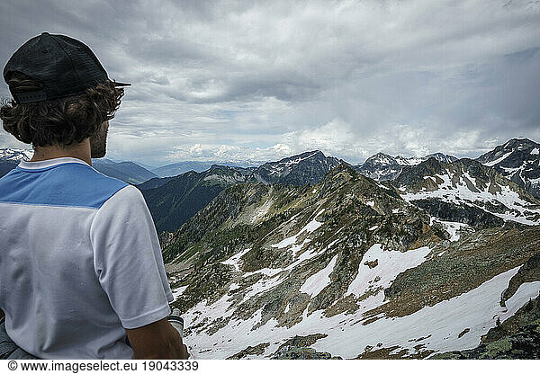 Young man stands  looking at mountain with a cloudy sky  BC  Canada
