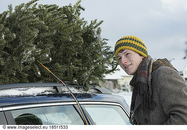 Young man strapping the Christmas tree on the roof of his car  Bavaria  Germany