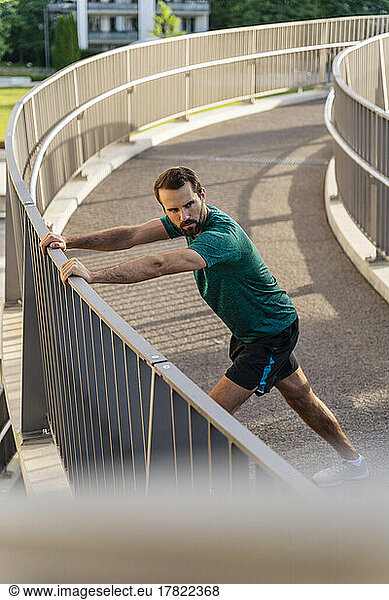 Young man stretching on footbridge