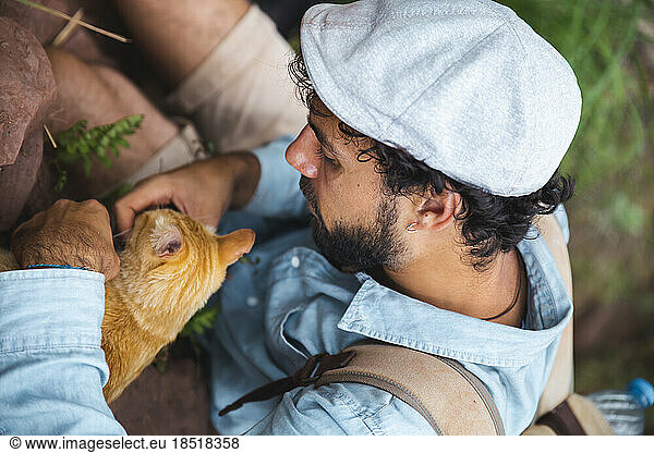 Young man stroking cat in forest