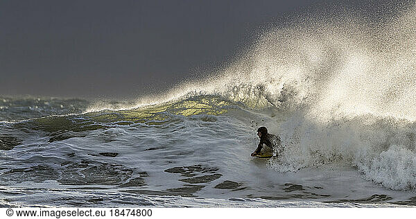 Young man swimming with surfboard in wavy sea on vacation