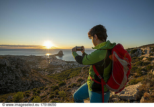 Young man take pictures at sunrise over rocky landscape Costa Blanca