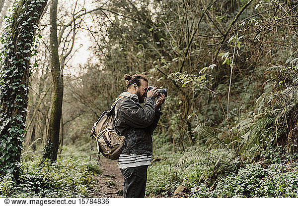 Young man taking pictures in the forest with his camera
