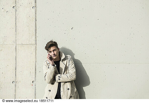 Young man talking on mobile phone and leaning against concrete wall  Munich  Bavaria  Germany