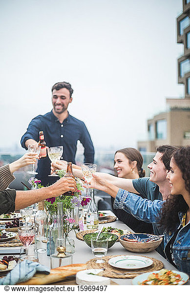 Young man toasting drinks with friends during social gathering on rooftop