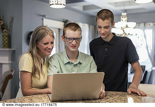 Young man uses a laptop computer at home with support from his mother and brother; Edmonton  Alberta  Canada
